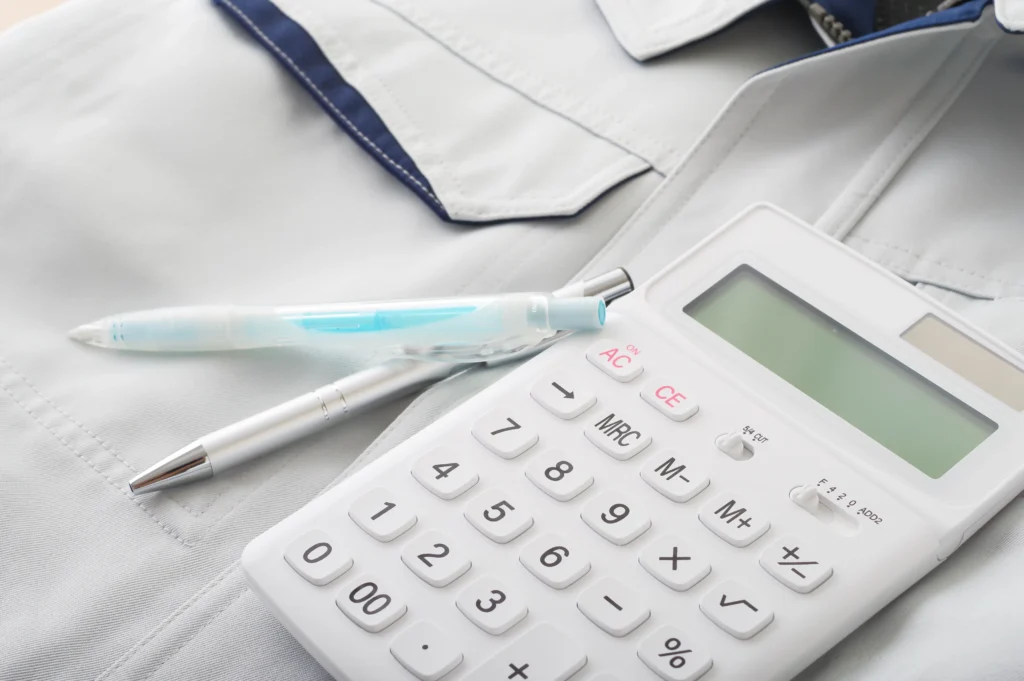 消防設備工事の費用をイメージする電卓とペン(作業着の上)