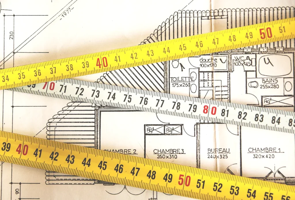 建築図面の上にメジャーを置いて寸法を測っているイメージ