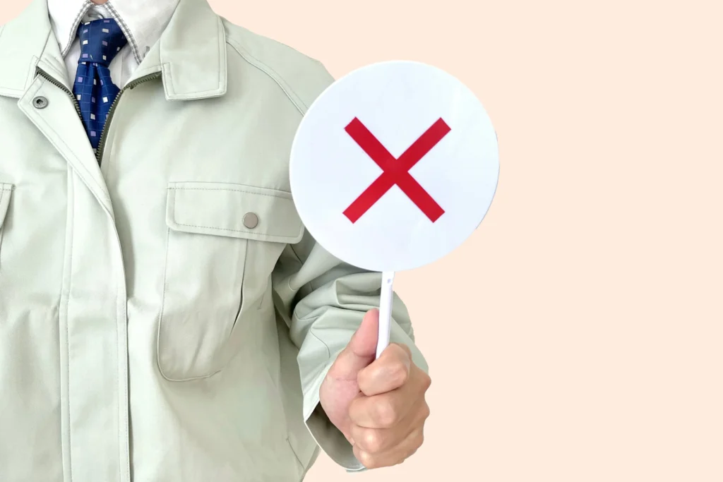 違反や不備を示す×印の札を持つ作業員(罰則・注意喚起のイメージ)